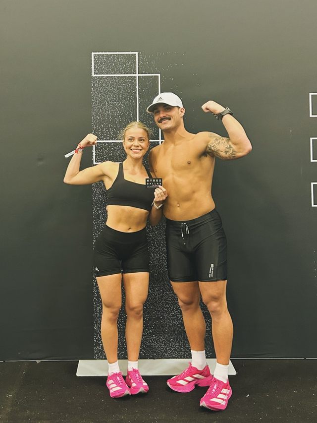 Hunter and Natalia flexing in front of the Hyrox Champions wall
